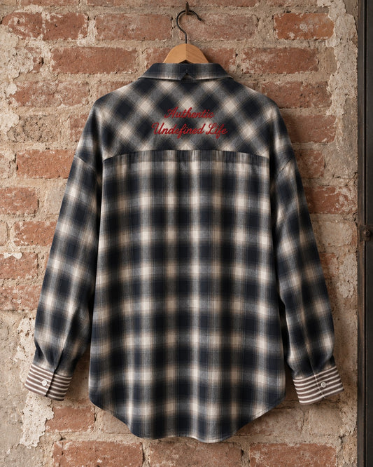 Camisa oversize de cuadro AÜL colgada en percha, espalda con bordado 'Authentic Undefined Life' en rojo