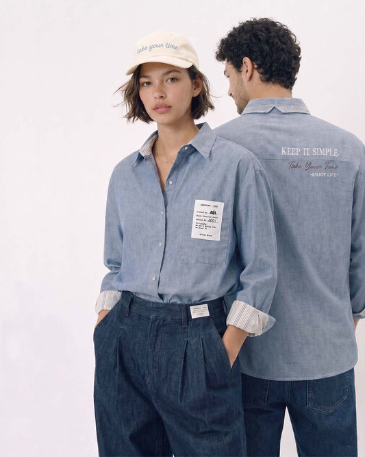 Camisa unisex oversize con tejido algodón efecto denim y contraste en interior cuello y puños con un tejido de rayas, fit relajado estilo minimalista y moderno y urbano. estampado en la espalda y en el bolsillo delantero una etiqueta con número de serie exclusivo y personalizado