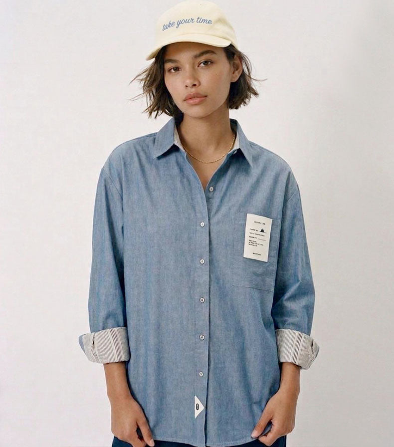 Camisa unisex de estilo  oversize con tejido algodón efecto denim y contraste en interior cuello y puños con un tejido de rayas, fit relajado estilo minimalista y moderno y urbano. estampado en la espalda y en el bolsillo delantero una etiqueta con número de serie exclusivo y personalizado