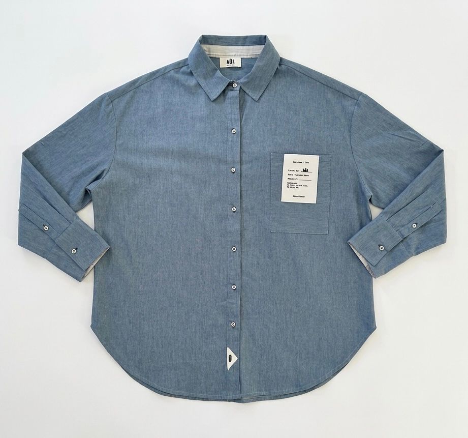 Camisa unisex de estilo  oversize con tejido algodón efecto denim y contraste en interior cuello y puños con un tejido de rayas, fit relajado estilo minimalista y moderno y urbano. estampado en la espalda y en el bolsillo delantero una etiqueta con número de serie exclusivo y personalizado